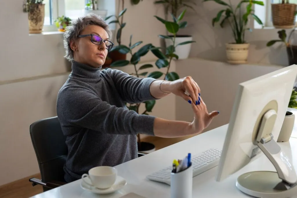 Mujer trabajando estirándose frente a su computadora.